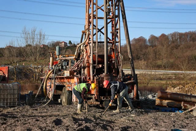 Yeraltı petrol sondajı ve inşaat çalışması yapan işçiler, büyük sondaj makinesi önünde toprak kazıyor.