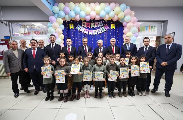 Neşeli çocuklar ve öğretmenler, balonlar ve kutlama süsleriyle dolu etkinlik alanında.