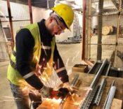 İşçi, güvenlik kaskı ve eldivenle metal montajı yaparken, atölyede güvenli çalışma ortamı sağlanıyor.